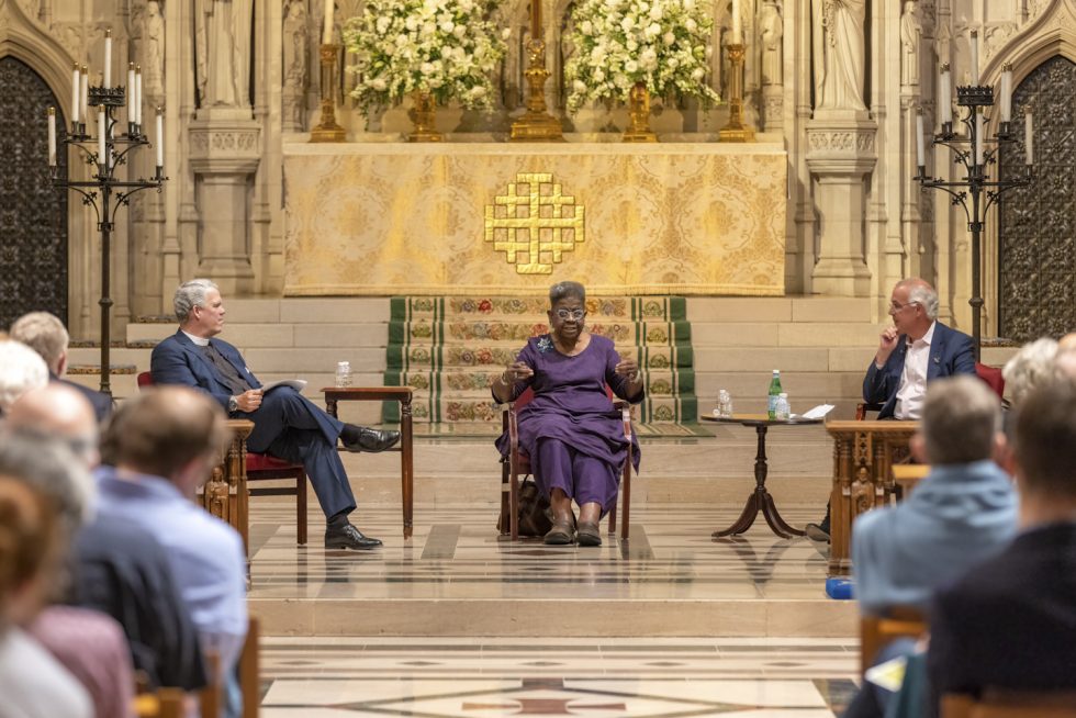Panelists sit before the Cathedral's high altar as an audience watches in the foreground.