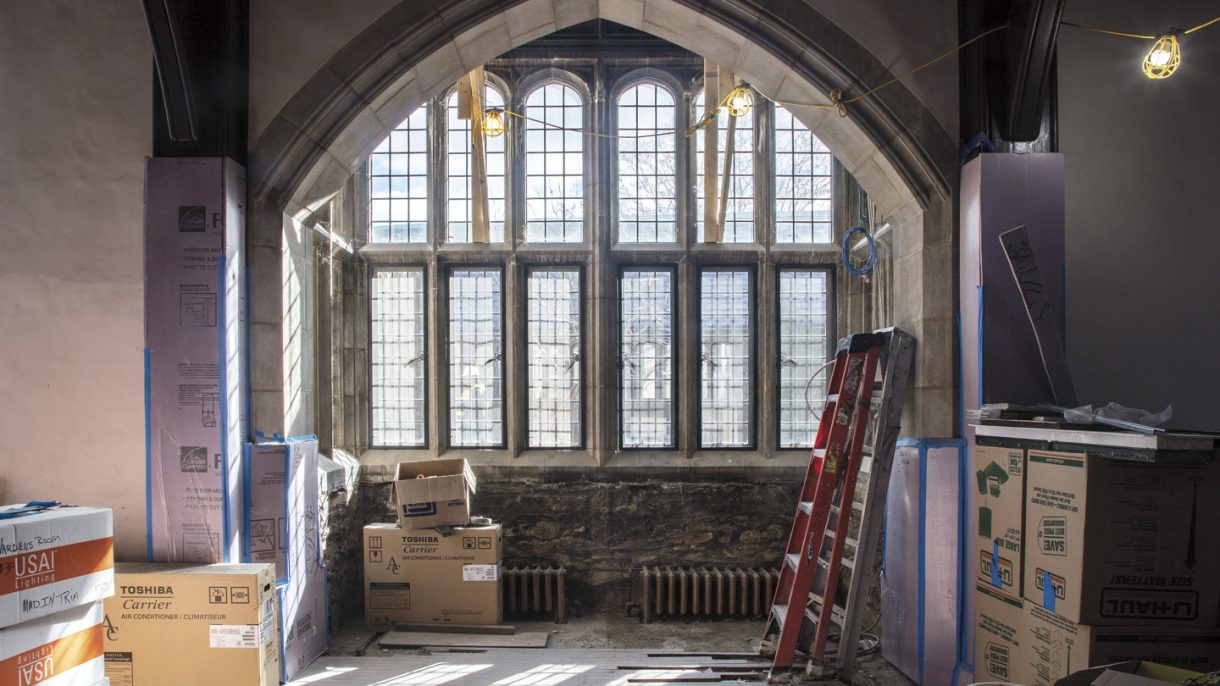 Construction equipment rests in front of a large gothic-style window.