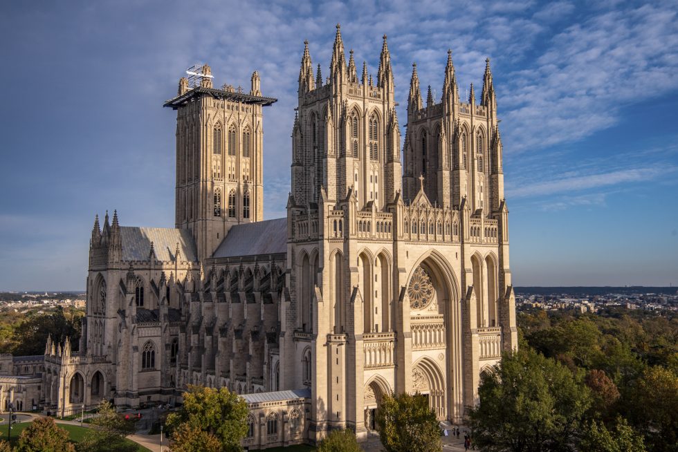 The gothic Cathedral's limestone architecture glows in the late afternoon sun in front of a blue sky.