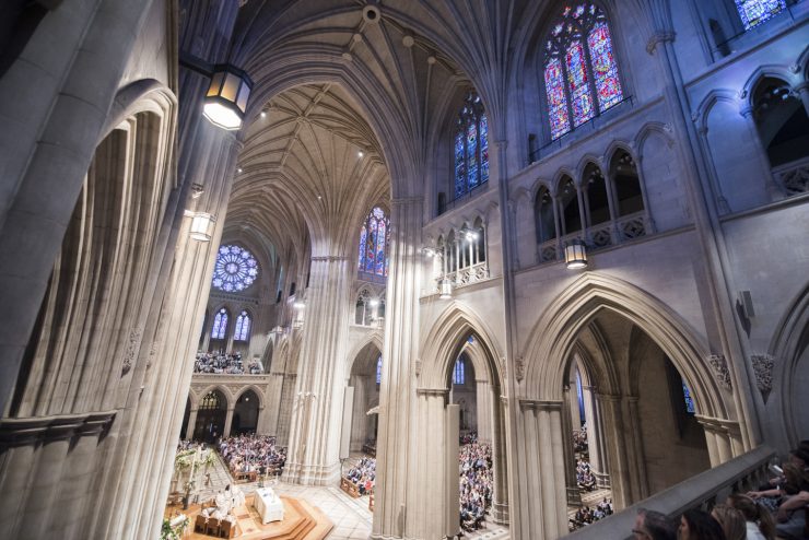 A wide interior view of the grand open nave of the National Cathedral during a worship service.