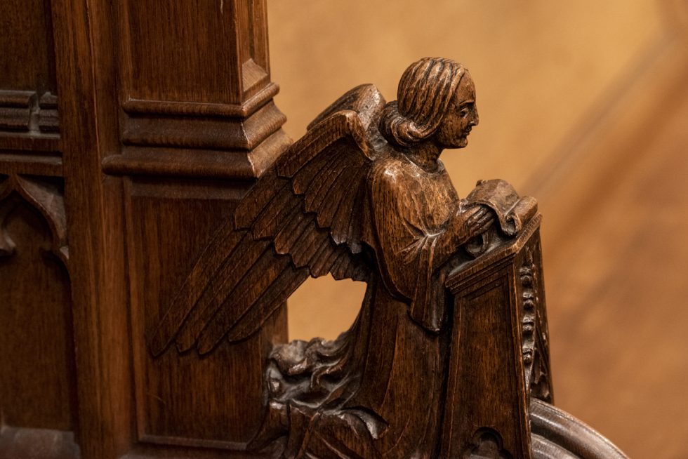 An intricate wood carving depicting an angel adorns the end of a long wooden bench.