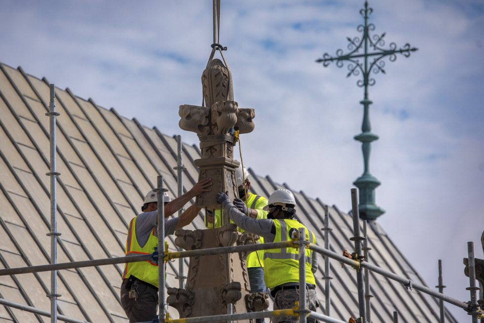 Stone masons high atop scaffold place a restored pinnacle.