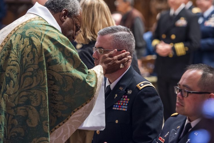 Presiding Bishop Michael Curry blesses a man in military uniform at a worship service.
